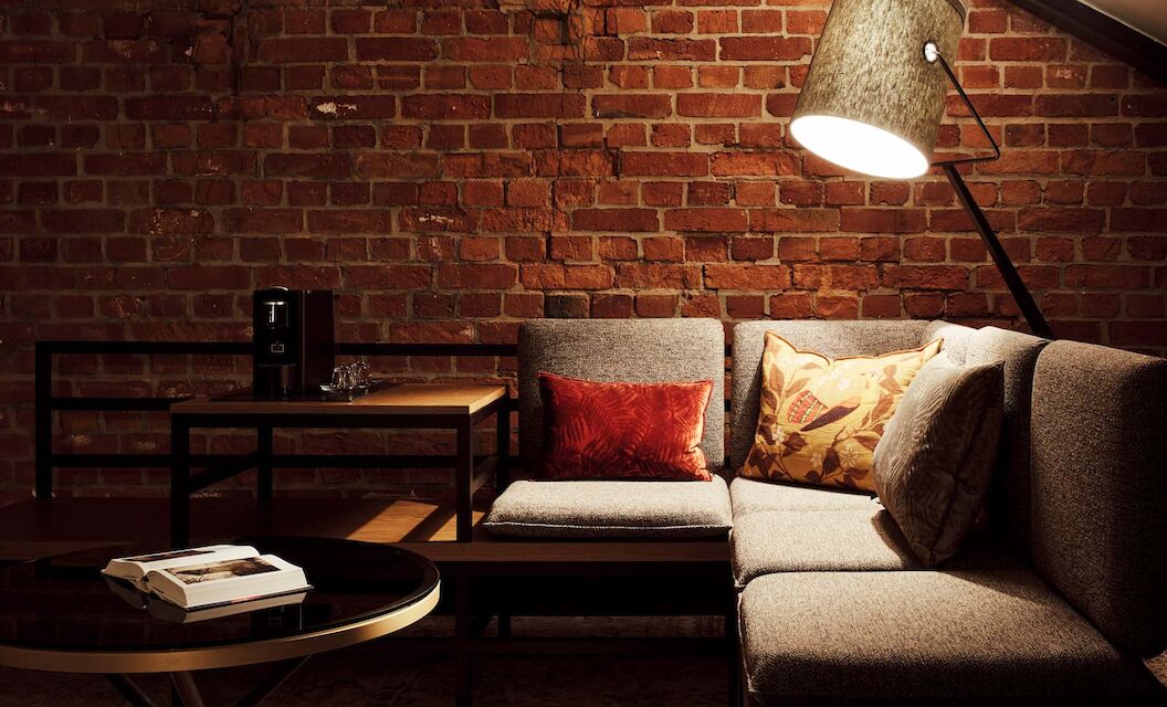 L-Loft mit Sitzbereich, Stehlampe und sichtbarer Backsteinwand