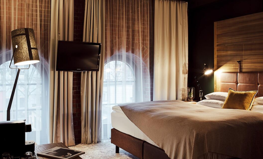 Bett, große Fensterfront mit Backsteinwand, Fernseher und Stehlampe