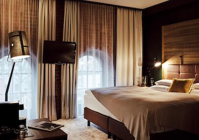 Bett, große Fensterfront mit Backsteinwand, Fernseher und Stehlampe