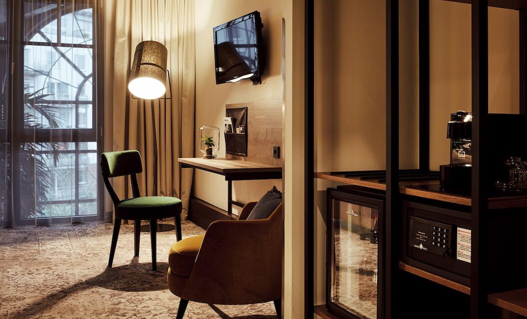 Zimmer mit Schreibtisch, TV, Sessel, Wandregal, Minibar und Safe
