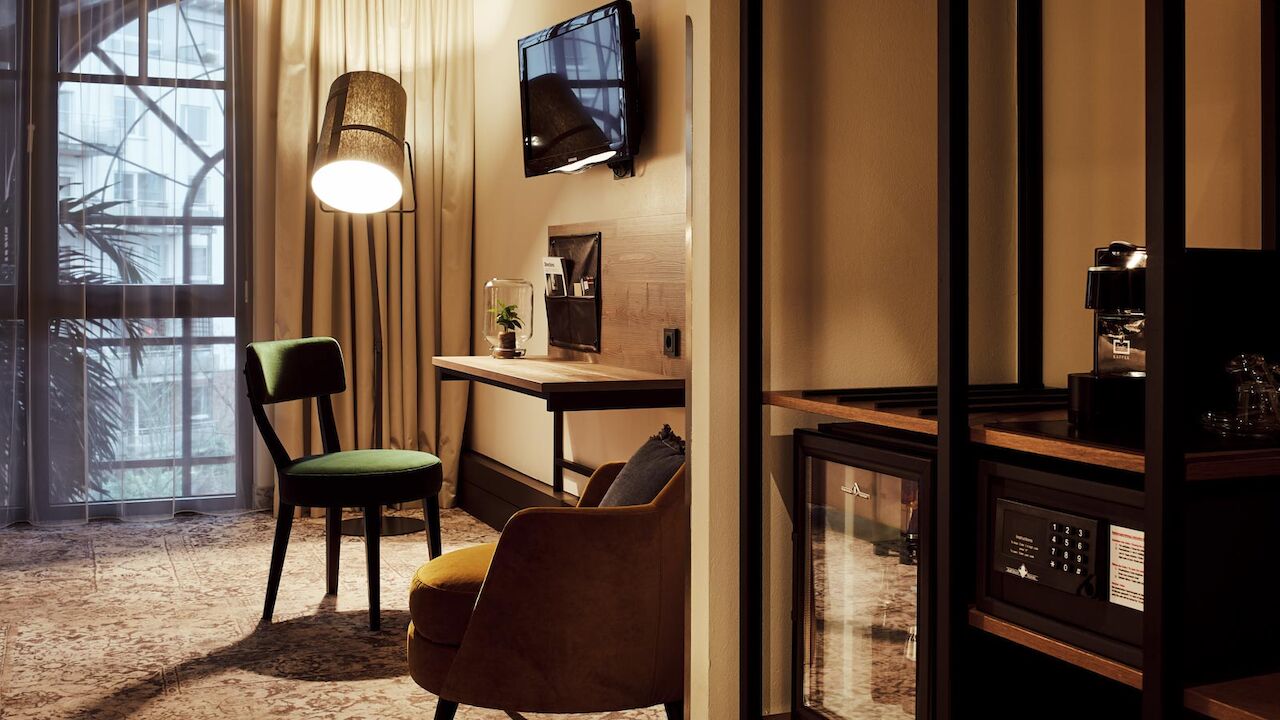 Zimmer mit Schreibtisch, TV, Sessel, Wandregal, Minibar und Safe