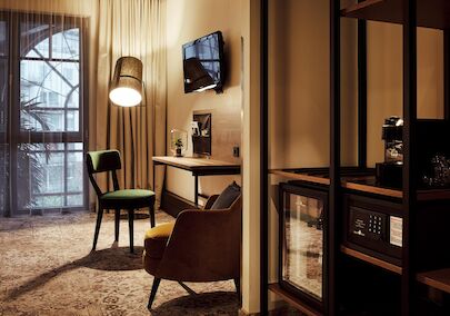 Zimmer mit Schreibtisch, TV, Sessel, Wandregal, Minibar und Safe