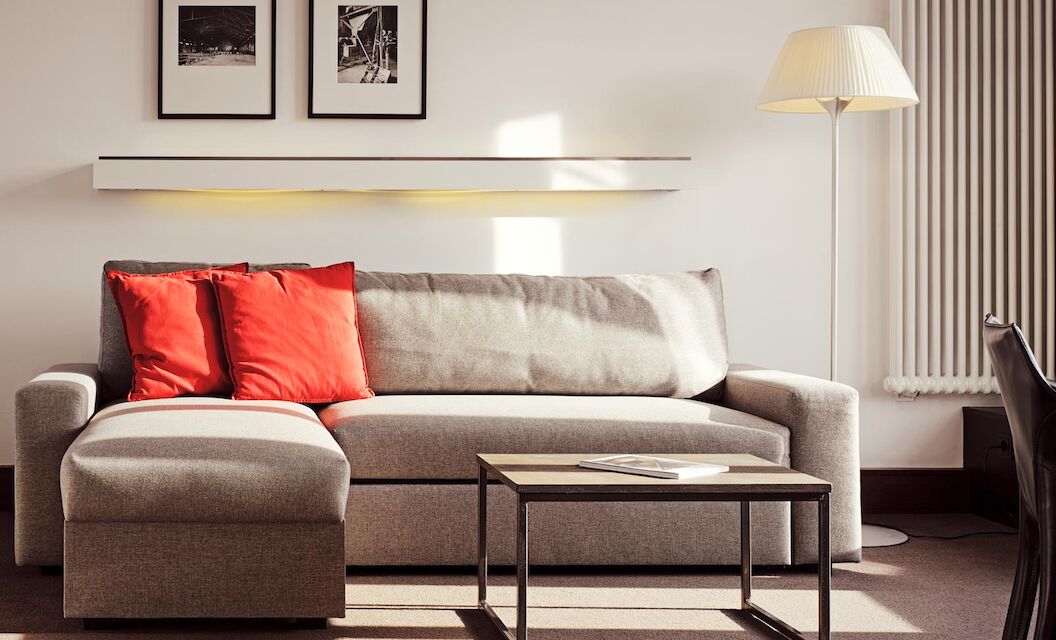 Graues Sofa mit Recamiere und roten Kissen, davor ein Beistelltisch