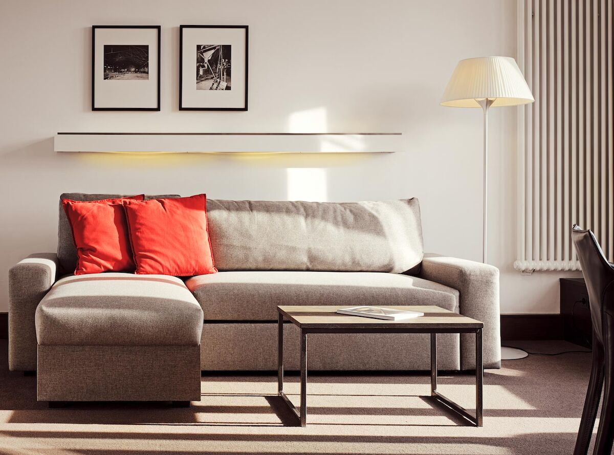 Graues Sofa mit Recamiere und roten Kissen, davor ein Beistelltisch