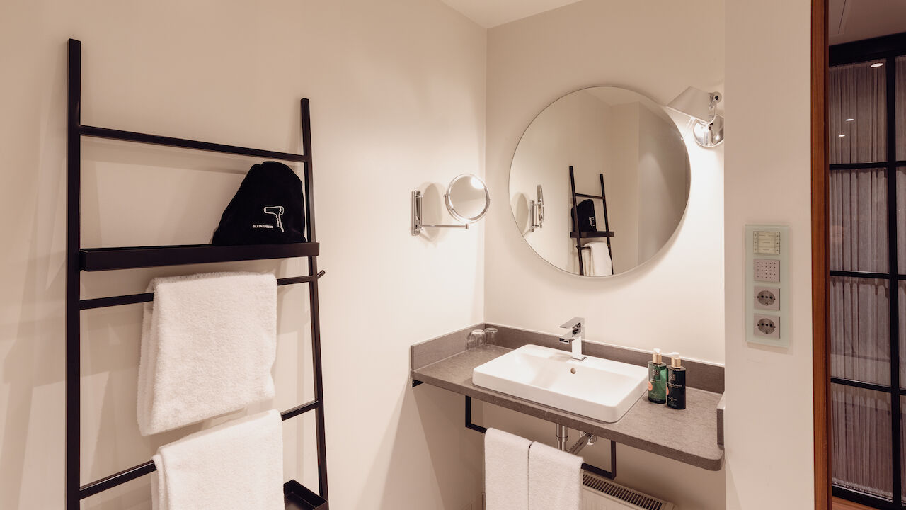 Das Badezimmer aus dem Gastwerk Hotel Hamburg M Loft Superior mit einem runden Spiegel.