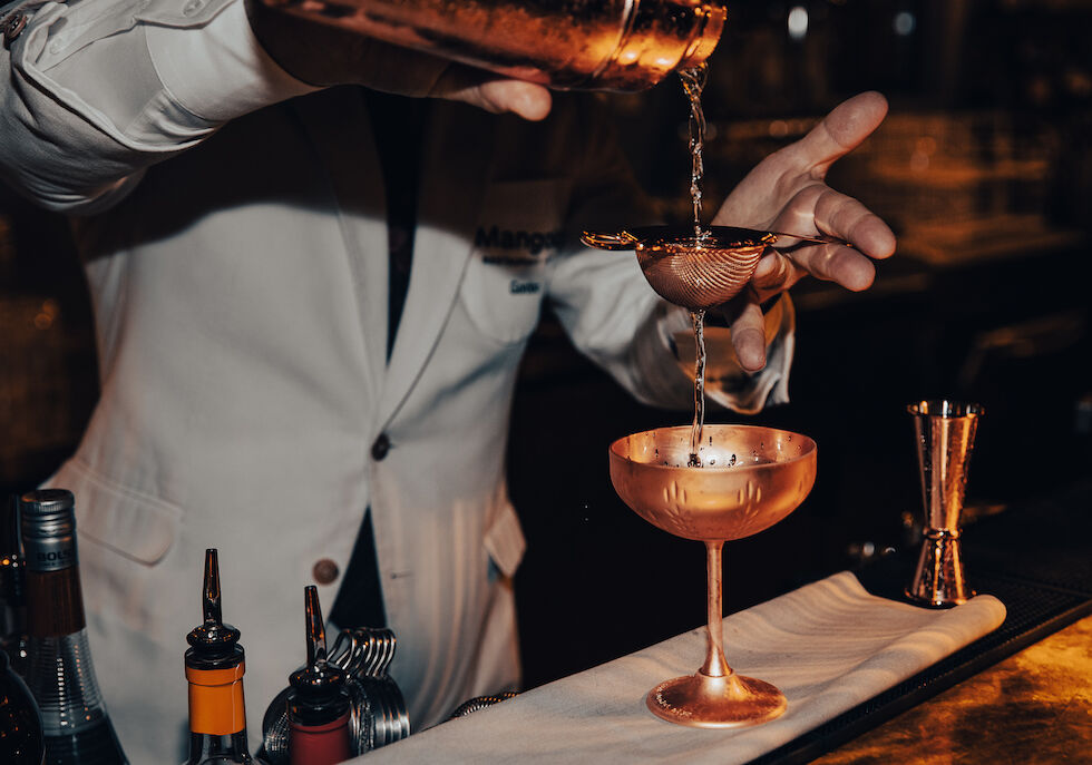 Bartender strains drink into a brass cocktail shaker