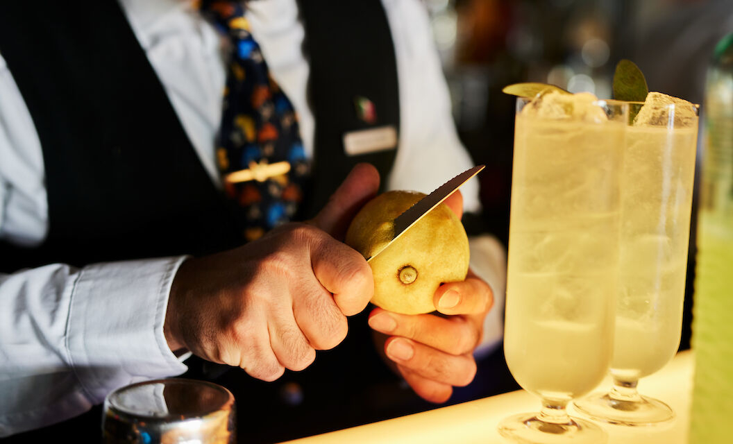 The George Hotel Hamburg Bar Dacaio Moods 03 Bartender slicing lemon zest, two drinks in foreground