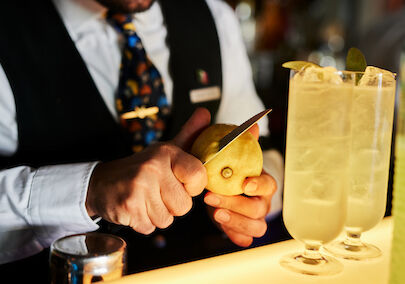 The George Hotel Hamburg Bar Dacaio Moods 03 Bartender slicing lemon zest, two drinks in foreground