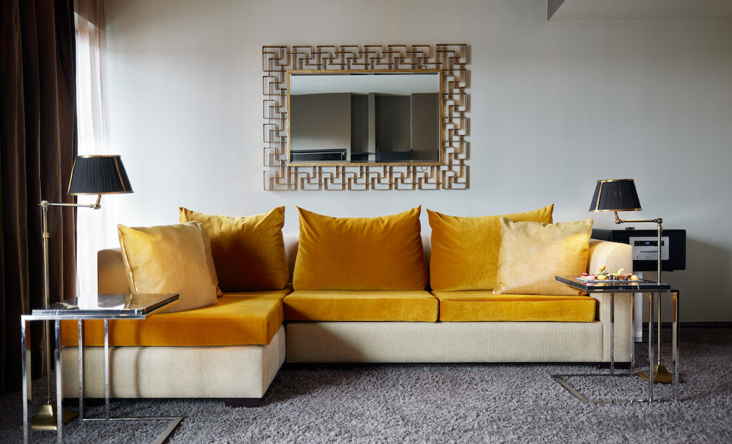 Large mustard sofa in front of mirror in hotel suite
