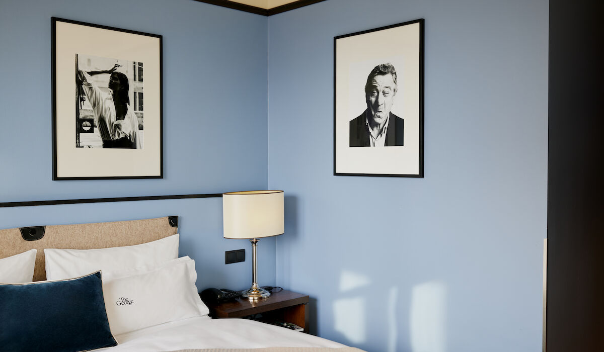 Doppelbett vor blauer Wand samt Foto eines Mannes an der Wand