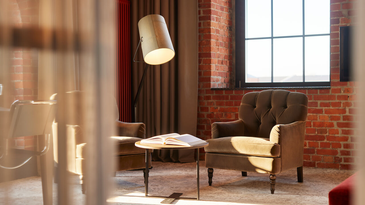 Edle Sessel, Stehlampe und Tisch mit Buch vor Backsteinwand im XL Loft