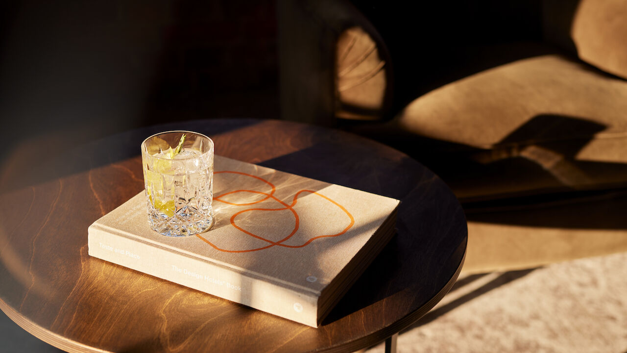 Design Hotels Buch und Drink auf Beistelltisch in der Sonne.