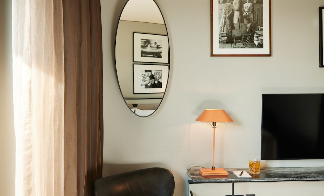 Partial armchair, mirror shows wall pictures, lamp on table by TV