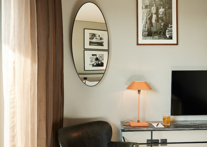 Partial armchair, mirror shows wall pictures, lamp on table by TV