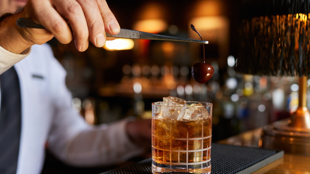 Drink im Tumblerglas wird mit einer Kirsche garniert.