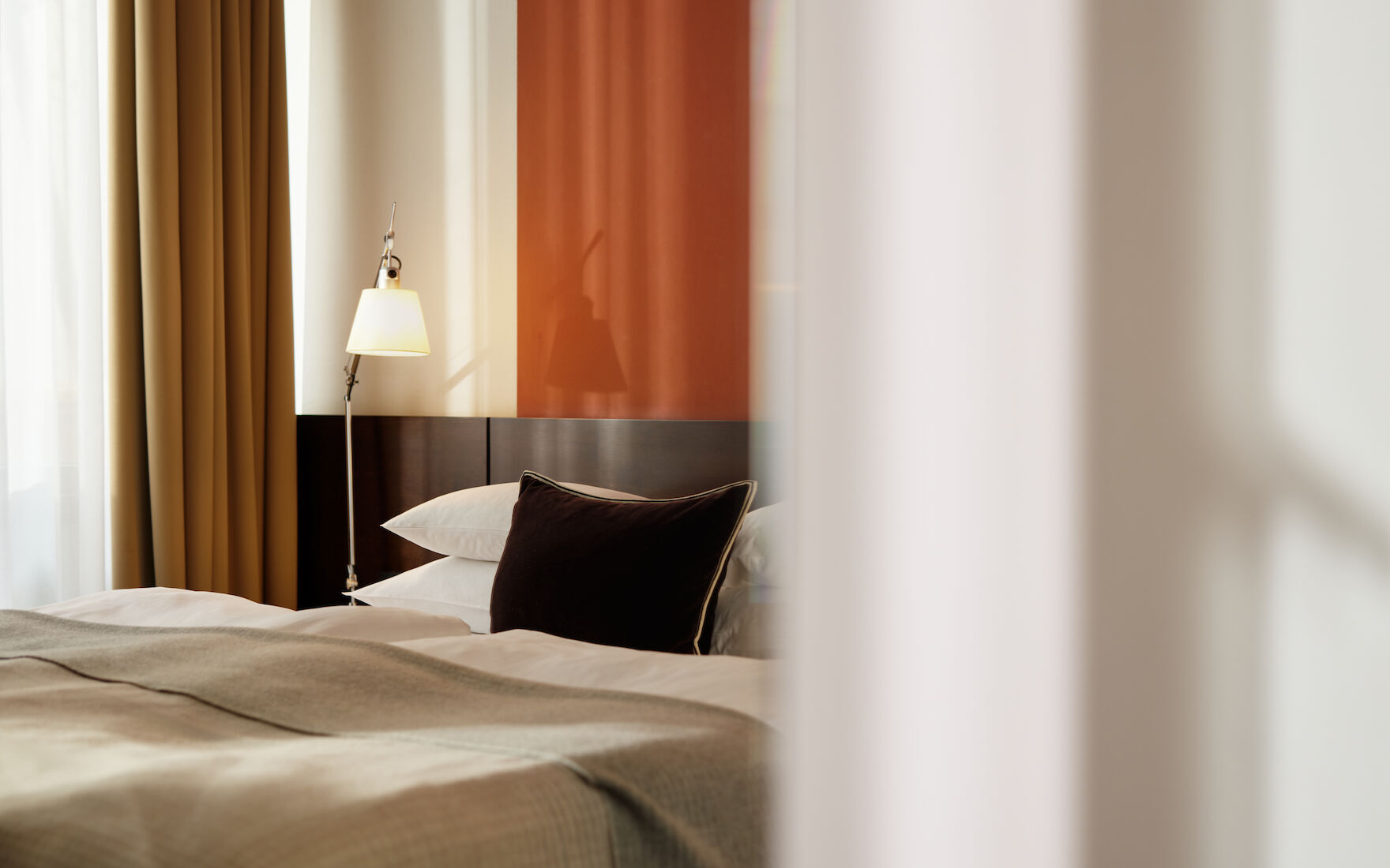 Seitlicher Blick auf Doppelbett im M Loft mit Gardine im Vordergrund