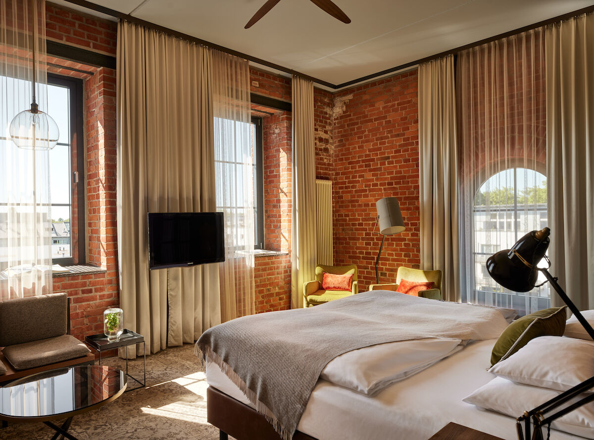 L Loft des Gastwerk Hotel Hamburg mit Bett, Backsteinwand und gelben Sesseln