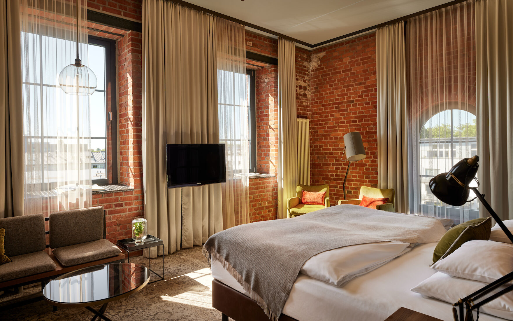 L Loft des Gastwerk Hotel Hamburg mit Bett, Backsteinwand und gelben Sesseln