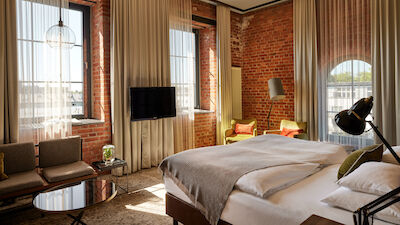 L Loft des Gastwerk Hotel Hamburg mit Bett, Backsteinwand und gelben Sesseln