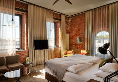 L Loft des Gastwerk Hotel Hamburg mit Bett, Backsteinwand und gelben Sesseln