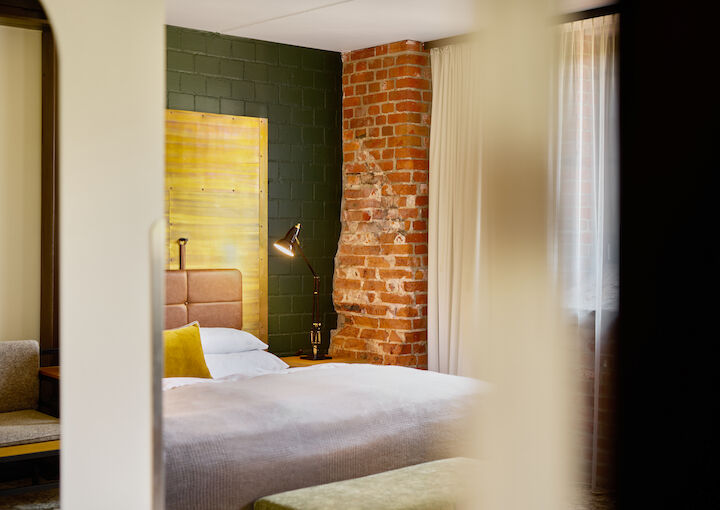 L Loft mit großem Bett im Anschnitt und Backsteinwand im Hintergrund